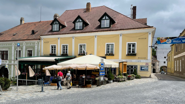 Rathskeller Weitra, © Matthias Bachofner Ein gelbes Gebäude mit der Aufschrift 'Gasthof Hotel Cafe' in Weitra, Österreich. Vor dem Gebäude sind Tische mit Sonnenschirmen und Passanten zu sehen.