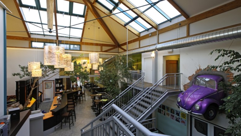 Fit Aktivcenter, © Fit Aktivcenter Innenansicht eines modernen Fitnesscenters mit Glasdach, Barbereich und lila VW Käfer an der Wand.