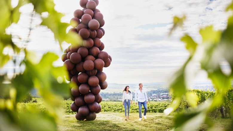 Giant bunch of grapes along the wine trail, © © Waldviertel Tourismus, Gerhard Wasserbauer Two people walk next to a large sculpture, the giant bunch of grapes, along the wine trail in the vineyards.