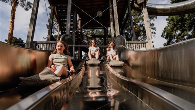 Kittenberger Erlebnisgärten, © Matthias Streibel Drei Kinder rutschen auf einer Metallrutsche in einem Park.