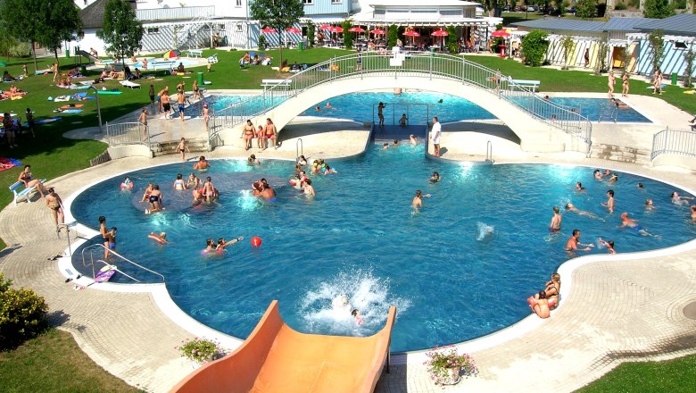 Freibad Hadersdorf, © Gemeinde Hadersdorf Freibad mit Pool, Brücke und Rutsche, viele Menschen beim Schwimmen und Sonnenbaden.