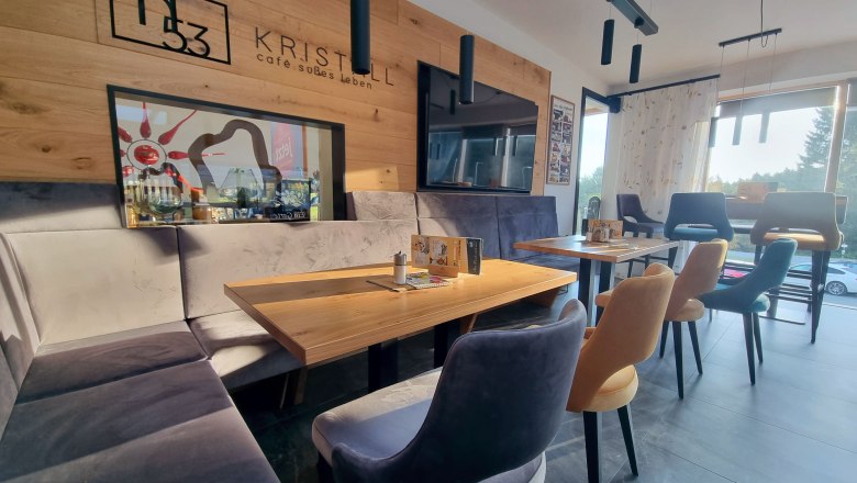 Sonnengarten im Café Kristall, © Café Pension Kristall Innenansicht eines modernen Cafés mit Holzwänden, bequemen Stühlen und großen Fenstern, die Sonnenlicht hereinlassen.