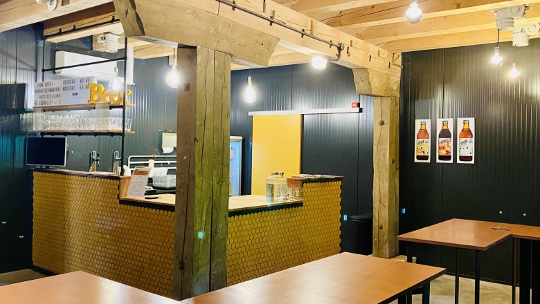 Shop, © Hopfenspinnerei Innenansicht eines modernen Cafés mit Holzbalken, Bartresen und hohen Tischen.