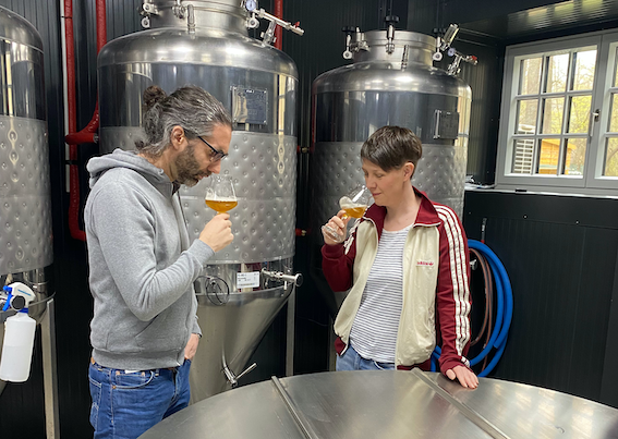 Qualitätskontrolle, © Hopfenspinnerei Innenansicht eines modernen Cafés mit Holzbalken, Bartresen und Tischen.