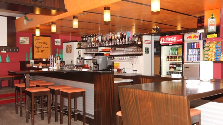 Auberg Pub_01, © Auberg Pub Innenansicht einer Bar mit Holzmöbeln, Barhockern und Getränken.