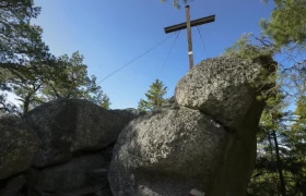 Hoher Stein, © Matthias Schickhofer Große Felsen mit einem Holzkreuz auf einem bewaldeten Hügel.