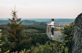 Nebelstein, © Waldviertel Tourismus, sommertage.com Eine Person steht auf einer Aussichtsplattform und blickt über einen bewaldeten Hügel bei Sonnenuntergang.