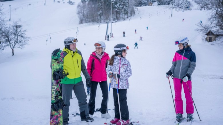 Arralifte Harmanschlag, © Waldviertel Tourismus, Robert Herbst Gruppe von Skifahrern und einem Snowboarder auf einer verschneiten Piste mit Skilift im Hintergrund.