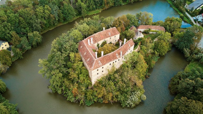 Burg Burgschleinitz, © Waldviertel Tourismus, lichtstark.com Luftaufnahme einer von Wasser umgebenen Burg mit roten Dächern und umgebenden Bäumen.