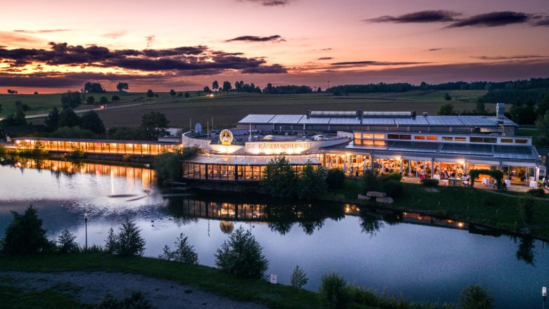 The world of cheesemaking, © Kaskuchl Cheese maker's world building at sunset, illuminated and situated on the water.