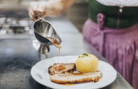 Hausmannskost von Karpfen bis Sonntagsbraten, © Niederösterreich Werbung/David Schreiber Eine Person gießt Soße über einen Teller mit Braten und Knödel.