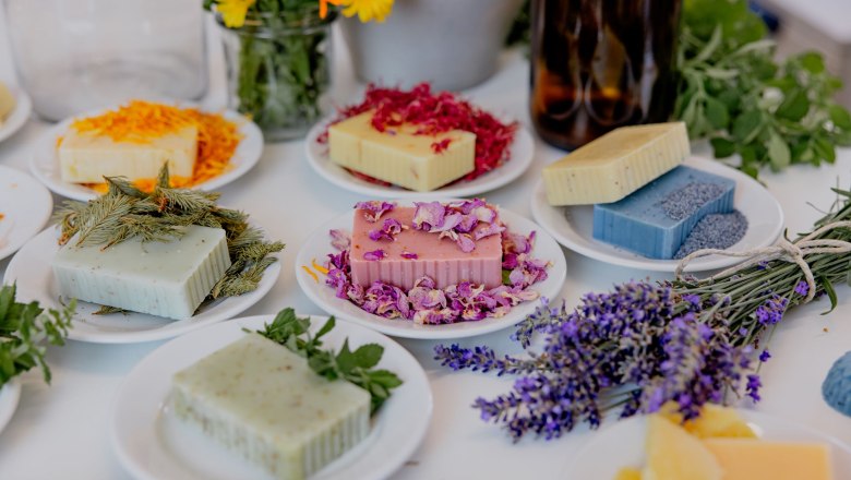 Seifen sieden, © Waldviertel Tourismus, Matthias Streibel Verschiedene handgemachte Seifen auf Tellern mit Blumen und Kräutern dekoriert.