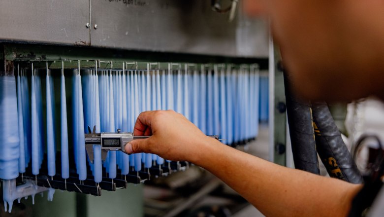 Pointed candle dunk system, © Waldviertel Tourismus, Matthias Streibel A person measures the thickness of blue candles with calipers in a factory.