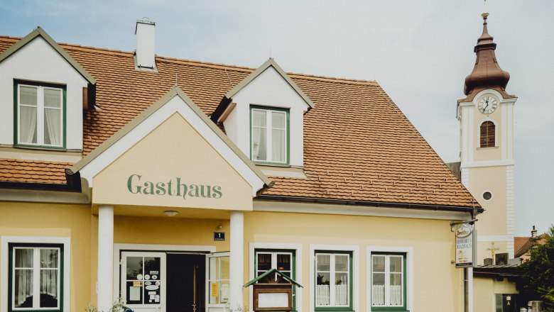 Wirtshaus in Japons, © Niederösterreich Werbung/Rita Newman Ein gelbes Gasthaus mit roten Dachziegeln und einem Kirchturm im Hintergrund.