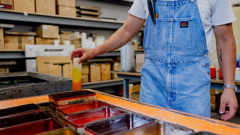 Coloring candles, © Waldviertel Tourismus, Matthias Streibel Person in dungarees dips candle in paint bath.