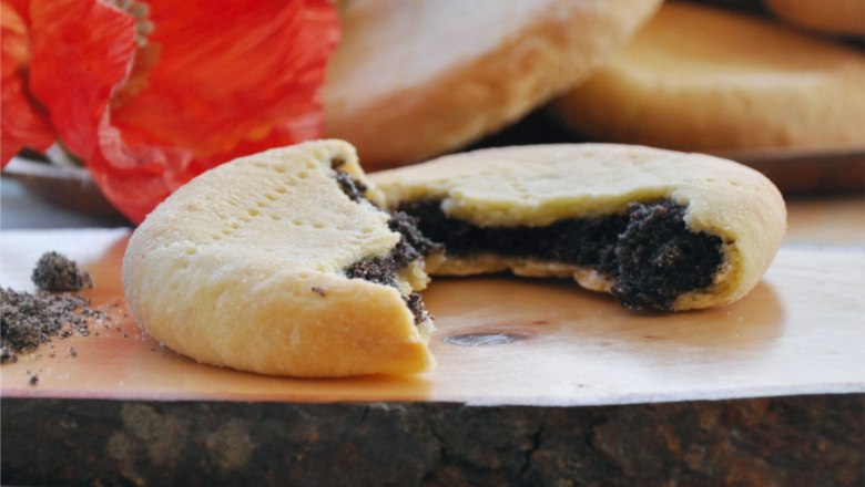 Mohnzelten, © Café Pension Kristall Ein aufgeschnittenes Mohnzelt mit Mohnfüllung auf einem Holzbrett, im Hintergrund eine rote Mohnblume.