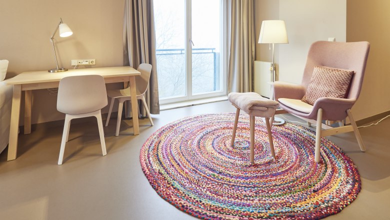 Haus Rosalia im Kloster Pernegg, © Schewig Dieter Helles Zimmer mit Schreibtisch, Stuhl, Sessel und buntem Teppich.