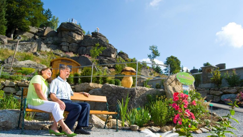Herb garden, © Marktgemeinde Bad Traunstein A couple sits on a bench in a herb garden with rocks in the background.