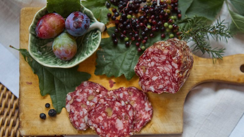 Salami, © esiphotography Nahaufnahme einer Salami auf einem Holzbrett mit Beeren und Pflaumen.