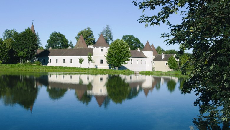 Marktgemeinde Pölla, © Marktgemeinde Pölla Schloss mit spitzen Türmen spiegelt sich in einem ruhigen See, umgeben von Bäumen.