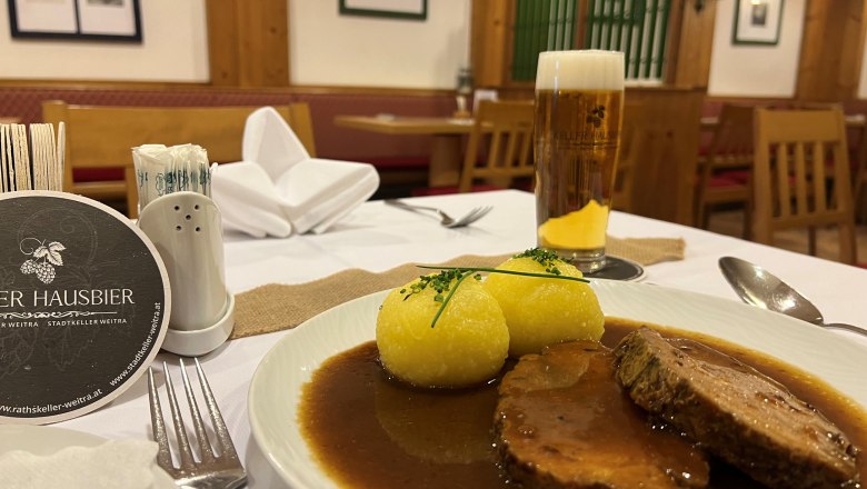 Roast pork with potato dumplings, © Matthias Bachofner A plate of roast pork and two potato dumplings in a restaurant, with a glass of beer next to it.