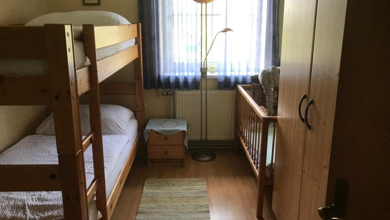 Kinderzimmer, © Ferienwohnung Meindl-Grübling Kinderzimmer mit Etagenbett, Kinderbett, Schrank und Stehlampe.
