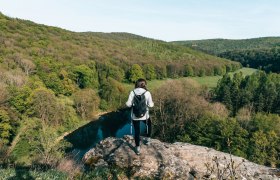 Nationalpark Thayatal, © Waldviertel Tourismus, sommertage.com Person mit Rucksack steht auf einem Felsen und blickt auf bewaldete Landschaft im Nationalpark Thayatal.