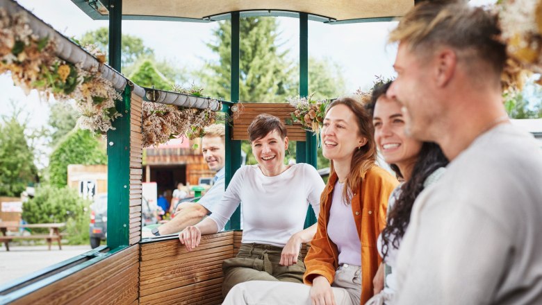 Mohnexpress, © © Waldviertel Tourismus, Gerhard Wasserbauer A group of people sit smiling in an open car decorated with flowers.