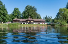 Strandbad Drosendorf, © Jovanov Ein Gebäude am Ufer eines Sees mit Bäumen im Hintergrund und Menschen, die das sonnige Wetter genießen.