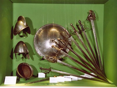 Waffen der Antonsammlung, © Zwettler Musuemsverein Ausstellung von antiken Waffen und Helmen in einem grünen Schaukasten.