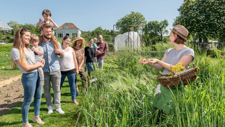 ARCHE NOAH, © Waldviertel Tourismus, Studio Kerschbaum Eine Gruppe von Menschen steht in einem Garten, während eine Frau mit einem Korb Pflanzen zeigt.