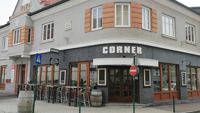 Corner Bar Horn, © Roman Zöchlinger Eckbar mit grauer Fassade und Holztüren, Tische und Fässer draußen.