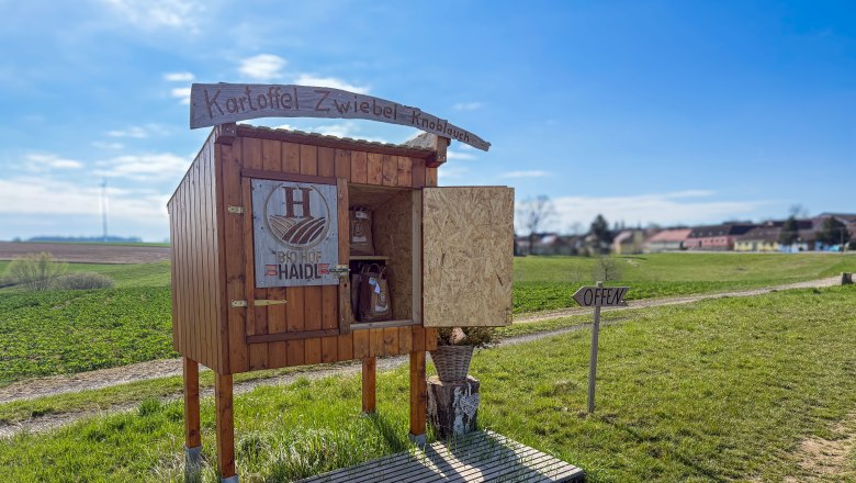 Farm-gate sale Haidl family, © Familie Haidl A small stall on a country lane with the inscription 'Kartoffel Zwiebel Knoblauch' and 'Bio Hof Haide'. A sign says 'Open'.