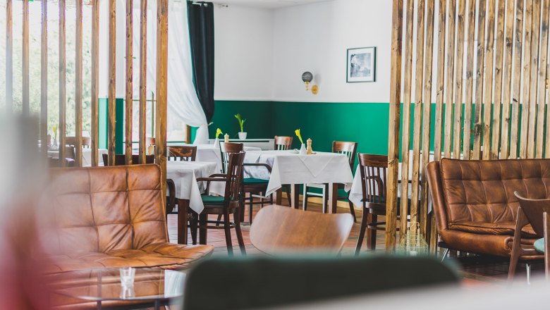 Gastraum, © Schlossschenke Ein stilvoll eingerichteter Gastraum mit Holzmöbeln, grünen Wänden und weißen Tischdecken.