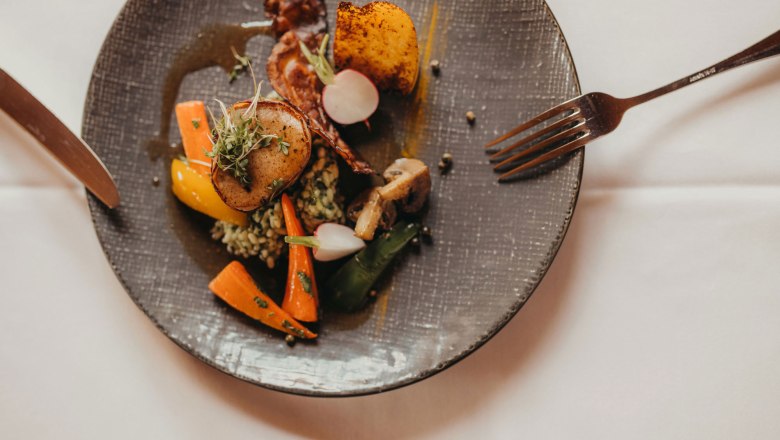 Pink pork fillet wrapped in pancetta with wild garlic risotto, © Niederösterreich Werbung/Daniela Führer A plate of pork fillet wrapped in bacon, wild garlic risotto, vegetables and potatoes.