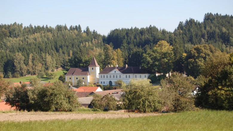 Marktgemeinde Waldhausen, © Marktgemeinde Waldhausen Ein Schloss mit gelbem Turm inmitten einer grünen Landschaft und umgeben von Bäumen.