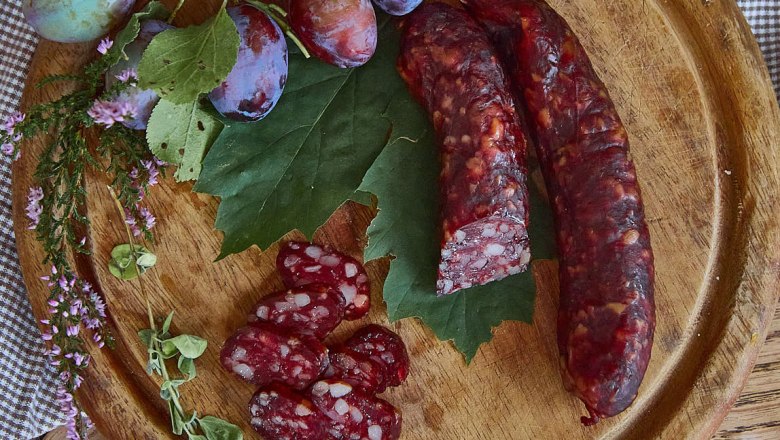 Kaminwurzn, © Amelie Seilern-Aspang Kaminwurzn und Pflaumen auf einem Holzbrett mit grünen Blättern und Kräutern dekoriert.