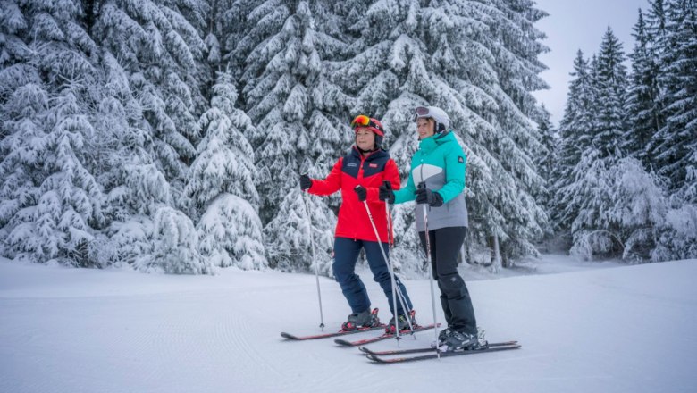 Schidorf Kirchbach, © Waldviertel Tourismus, Robert Herbst Zwei Skifahrer stehen auf einer verschneiten Piste vor schneebedeckten Bäumen.