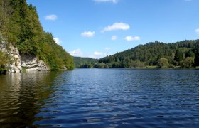 Stausee Thurnberg, © OEFG 1880 Ein ruhiger See umgeben von bewaldeten Hügeln unter blauem Himmel mit wenigen Wolken.