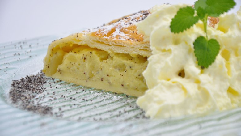 Weißmohn-Birnenstrudel, © Café Pension Kristall Ein Stück Weißmohn-Birnenstrudel mit Sahne und Minzblatt auf einem Teller.