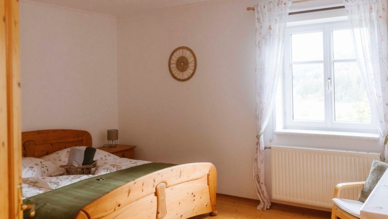 Doppelzimmer 2, © Katja Koppensteiner Fotografie Gemütliches Doppelzimmer mit Holzmöbeln und Fenster mit Vorhängen.