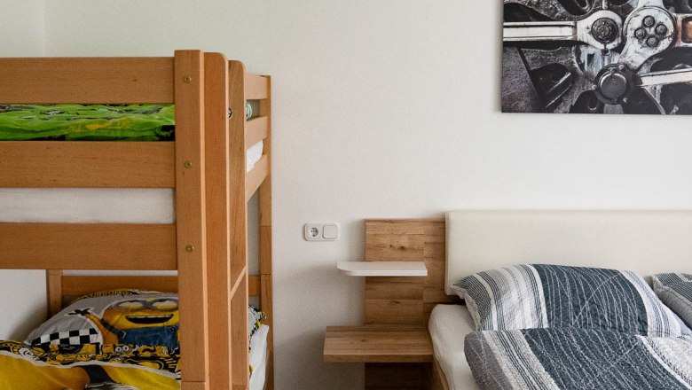 Bedroom (double bed + bunk bed), © Manuel Hahn A bedroom with a bunk bed and a double bed made of wood. A picture with a technical motif hangs on the wall.