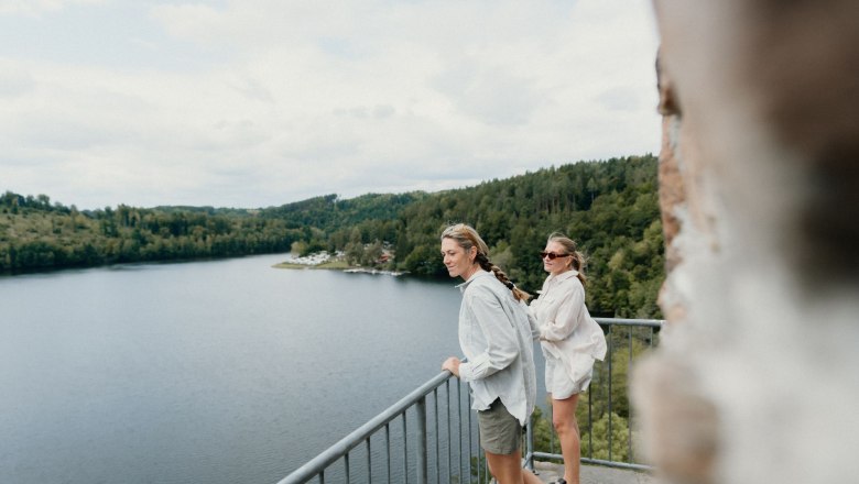 Ruine Dobra, © Niederösterreich Werbung, Patrick Wasshuber Zwei Frauen stehen auf einem Balkon mit Blick auf einen See und bewaldete Hügel.