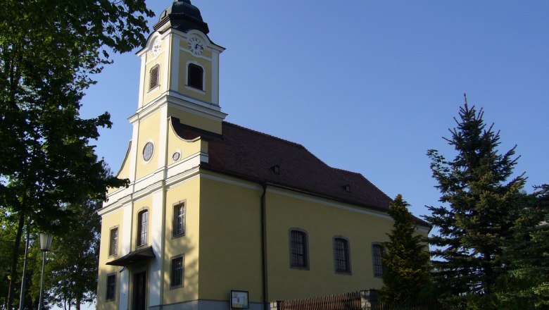 Pfarrkirche Haugschlag, © Gemeinde Haugschlag Pfarrkirche Haugschlag mit gelber Fassade und Turm, umgeben von Bäumen.