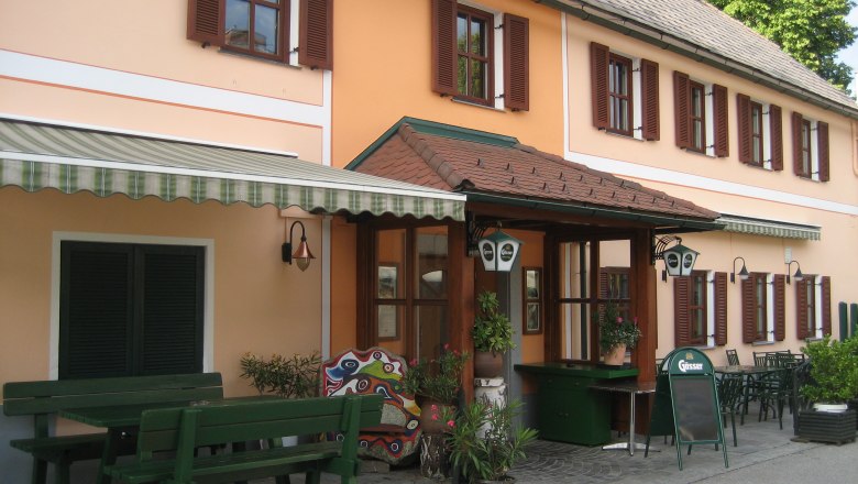 Gasthof Lichtenwallner, © Gasthof Lichtenwallner Eingang eines traditionellen Gasthofs mit orangefarbener Fassade und grünen Holzmöbeln im Freien.