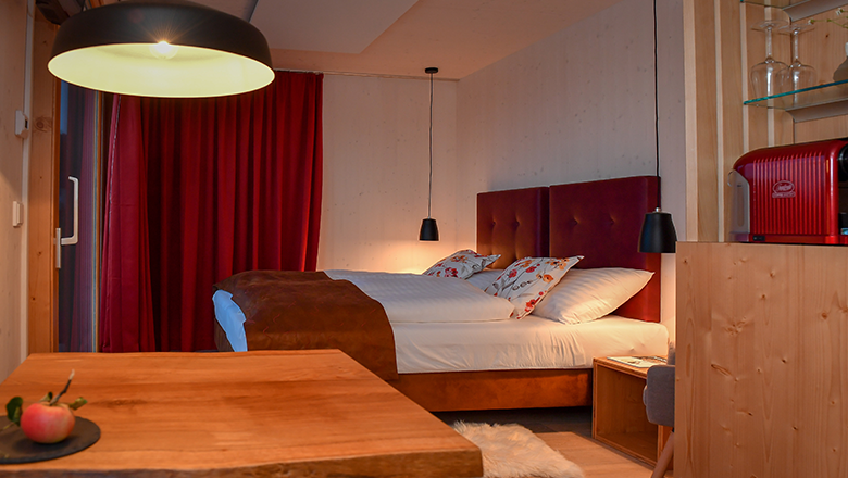 roon_zimmer3, © Franz Atteneder Gemütliches Hotelzimmer mit Doppelbett, rotem Vorhang und Holzmöbeln.