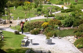 Schaugarten Kurt Zlabinger, © Kurt Zlabinger Ein gepflegter Schaugarten mit geschwungenen Wegen, Blumenbeeten und Gartenfiguren. Eine Person betrachtet die Pflanzen.