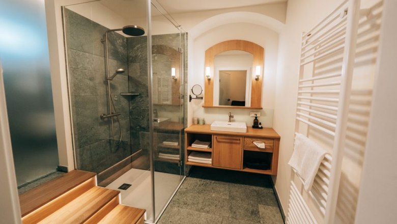 Zum Goldenen Löwen, © Zum Goldenen Löwen Modernes Badezimmer mit Glasdusche, Holzwaschtisch und Handtuchheizkörper.