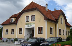 Gästehaus Hahn, © Gästehaus Hahn Gelbes Gästehaus mit rotem Dach und geparkten Autos davor.