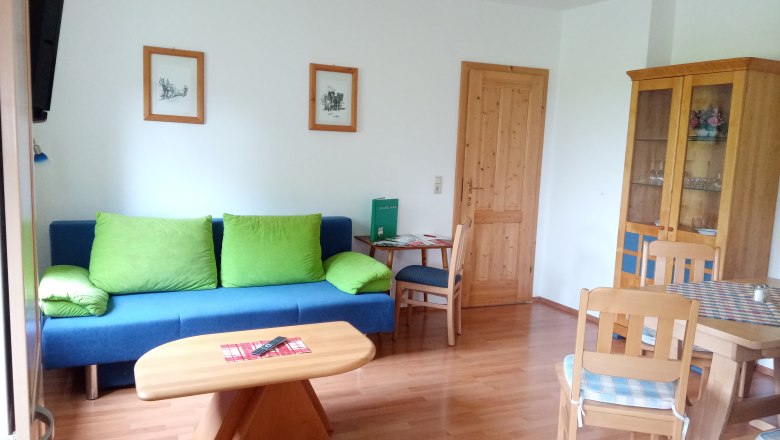 FW "Meadows & Fields", © Blumentalhof Living room with blue couch, wooden table and chairs, cupboard and pictures on the wall.